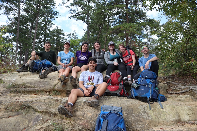 Eight students on a backpacking outdoor trip sitting on a large rock smiling.