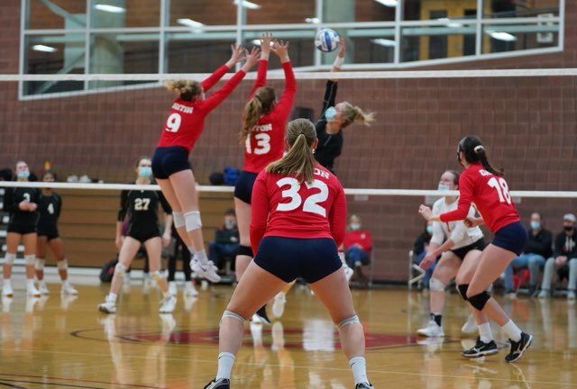 Two students block a hit in a women's club volleyball game. 